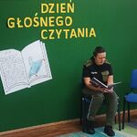 na zdjęciu kobieta w mundurze strazy granicznej czytajaca ksiązke, z tyłu duży zółty napis dzien głosnego czytania.jpg