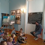 Grupa dzieci siedzi  na poduszkach przed przewodnikiem po muzeum 1.jpg