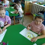 Grupka dzieci siedzi przy stoliku i koloruje na żółto szablon uśmiechniętej buźki 1.jpg