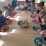 Dzieci siedzą przy stolikach i jedzą sałatkę owocową