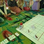 Dzieci siedzą na dywanie i obserwują poruszającego się po macie zaprogramowanego robota