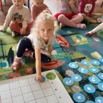 Dziewczynka układa na macie drogę Genibota do domku za pomocą symboli graficznych