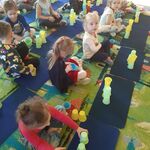 Dzieci siedzą na dywanie i układają wieżę z kolorowych kubeczków wg podanego kodu