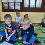 Dzieci siedzą na dywanie i na małych planszach układają sudoku