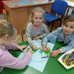 Troje dzieci przy stoliku koloruje  rysunek kuli ziemskiej.