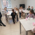 Dzieci stoją przy stolikach z akcoseriami przygotowanymi do wykonania odlewu herbu.jpg