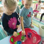 Dwoje dzieci barwi wodę w szklankach kawałkami kolorowej bibuły