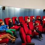 dzieci siedzą w czerwonych fotelach planetarium