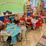 dzieci siedzą przy stolikach i ozdabiają drewniane choinki kredkami i mazakami lub farbami