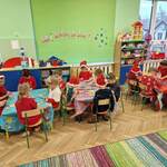 Dzieci siedzą na krzesełkach przy stolikach dekorując swoje choinki magnesowe