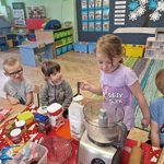 Dziewczynka łyżką wsypuje mąkę do miski robota kuchennego