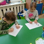 Dwoje dzieci siedzi przy stoliku i wypełnia karty pracy