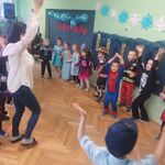 dzieci tańczą w kole. na pierwszym planie kobieta w białej bluizce unosząca ręce.jpg