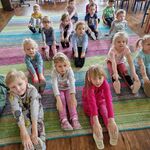 Dzieci siedzą na dywanie w siadzie prostym, przyjmując określoną pozycję 