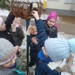 grupa dzieci wsypuje pokarm do karmnika_ z karmnika zwisają kawałki słoniny.jpg