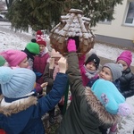 grupa uśmiechniętych dzieci wkładająca ziarna do drewnianego karmnika.jpg