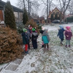 grupa dzieci ubrana w kurtki w ogrodzie przedszkolnym obok krzewów.jpg