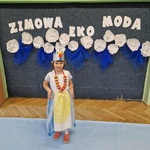 Dziewczynka pozuje do zdjęcia mając naszyjnik z nakrętek oraz koronę na głowie.