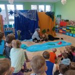 dwie aktorki w maskach zwierząt_ jedna myszka_ druga tygrys leżące na ziemi przy wodzie zrobionej z niebieskiego materiału.jpg