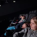kilkoro dzieci siedzi w kinowych fotelach. Na pierwszym planie dwie dziewczynki