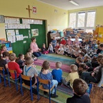 dzieci siedzą w kole na dywanie. Przed nimi nauczycielka