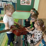 Dziewczynka trzymając gitarę pokazuje ją  innym dzieciom