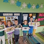 Grupa dzieci trzyma w dłoniach kartki na których znajdują się zdjęcia motyli.