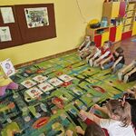 Dziewczynka prezentuje planszę z pozycją lwa Lolka_ pozostałe dzieci naśladują.