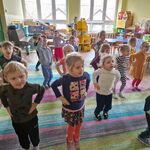 Dzieci stoją na dywanie z rękami na biodrach_ podskakują jak piłeczki.