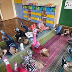 Dzieci leżą na dywanie na plecach i poruszając nogami naśladują jazdę rowerem