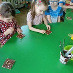 Kilkoro dzieci siedząc przy stoliku ozdabia czekoladowe wafle.