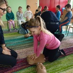 Dziewczynka ćwiczy pierwszą pomoc według instrukcji pani strażnik.