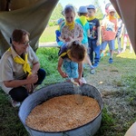 Dzieci ustawione przed namiotem biorą udział w konkursie na napełnianie butelki kukurydzą.