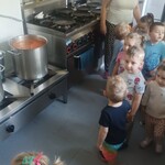 dzieci i pani obok wielkiego garnka z zupą i kuchenką z patelniami.j
