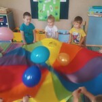 Dzieci trzymające chustę animacyjną nad którą unoszą się balony.jpg