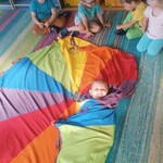 Uśmiechnięta dziewczynka leżąca na chuscie animacyjnej_ obok kilkoro dzieci.jpg