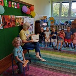 Mama siedzi obok córki i czyta dzieciom książkę.