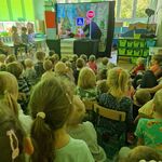 Na stole ustawione znaki drogowe_ dwóch aktorów prezentuje makiety samochodów.