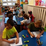 Dzieci siedzą przy stolikach i wykonują pracę plastyczną.