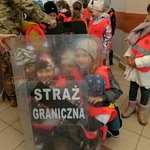 Kilkoro dzieci siedzi za tarczą funkcjonariusza.