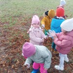 grupa dzieci zbiera liście z ziemi_ dziewczynka zakłada foliową rękawicę.j