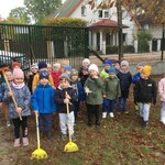 dzieci stoją na placu przedszkolnym_ troje z przodu trzyma grabie.