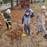 Chłopiec zagrabia liście_ a dwoje dzieci stoi z grabiami_ pozując do zdjęcia.
