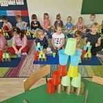 Dzieci siedzą w parach przed dywanikami i układają wieże wg przedstawionego wzoru
