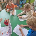 Dzieci siedzą przy stoliku i rozwiązują zadanie_ kolorując pola z cyfrą 1.