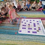 Dzieci siedzą na brzegu dywanu_ a dziewczynka układa kod za pomocą strzałek_ drogę kubka do pucharu