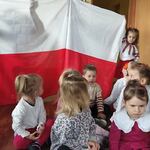 dwoje dzieci trzyma flagę Polski. Przed nimi inne dzieci