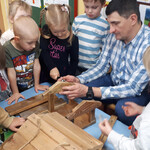 Dzieci patrzą jak dziewczynka z pomocą pana Dariusza skręca karmnik.