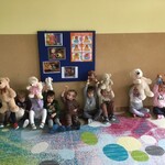10 dzieci siedzi pod ścianą trzymając w górze pluszowe misie.