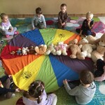 10 dzieci siedzi wokół chusty na której ułożone są w rzędzie misie od najmniejszego na największego.